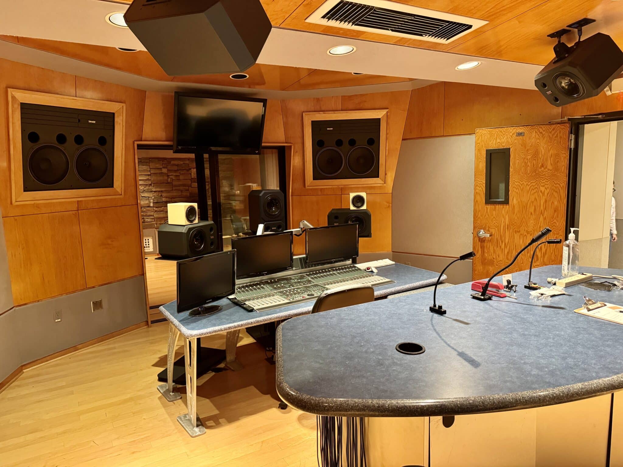 Wood-paneled recording studio control room with wall-mounted speakers, computer monitors, and a busy mixing desk area.